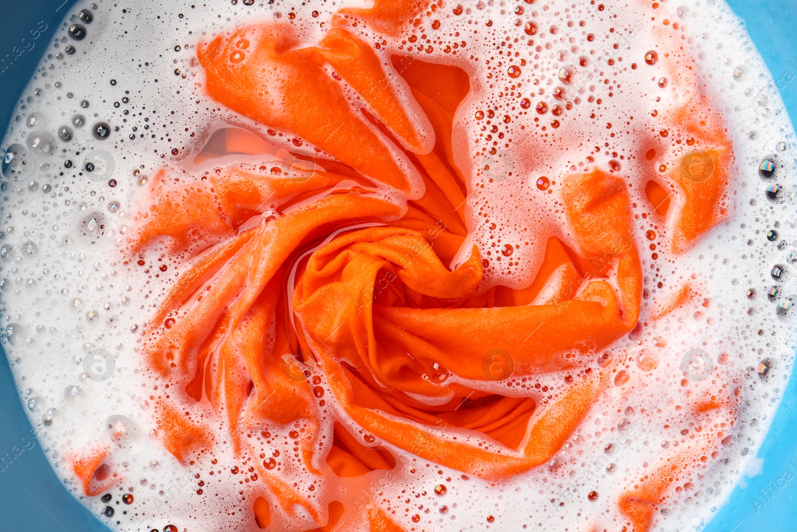 Photo of Orange clothes soaked in water before washing, top view