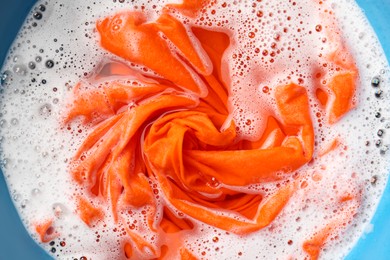 Photo of Orange clothes soaked in water before washing, top view