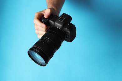 Photo of Photographer with professional camera on light blue background, closeup. Space for text