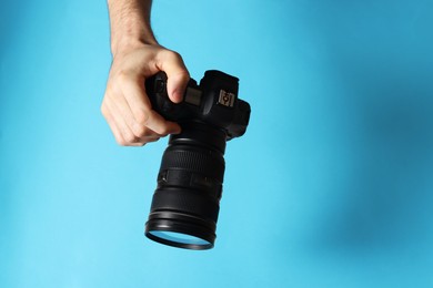 Photo of Photographer with professional camera on light blue background, closeup. Space for text