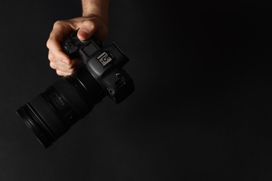 Photo of Photographer with professional camera on black background, top view. Space for text