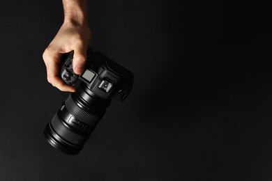 Photo of Photographer with professional camera on black background, top view. Space for text