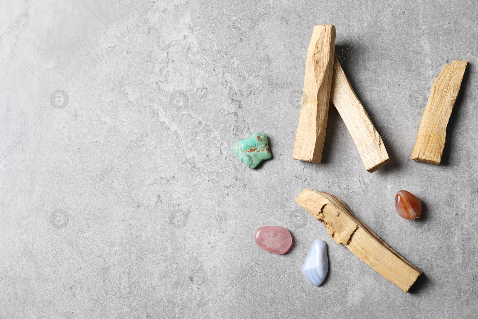 Photo of Palo santo sticks and gemstones on grey table, flat lay. Space for text