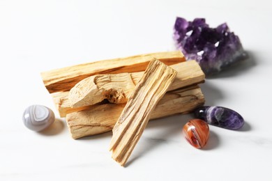 Photo of Palo santo sticks and gemstones on white table, closeup