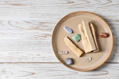 Photo of Palo santo sticks and gemstones on white wooden table, top view. Space for text