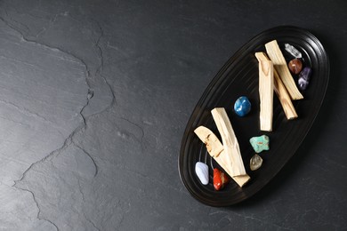 Photo of Palo santo sticks and gemstones on black table, top view. Space for text