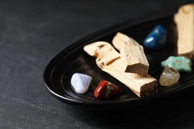 Photo of Palo santo sticks and gemstones on black table, closeup