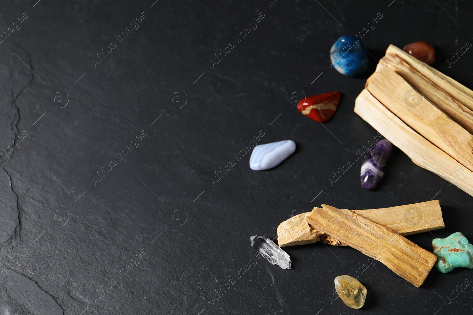 Photo of Palo santo sticks and gemstones on black table. Space for text