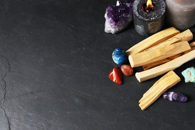 Photo of Palo santo sticks, gemstones and burning candles on black table, above view. Space for text