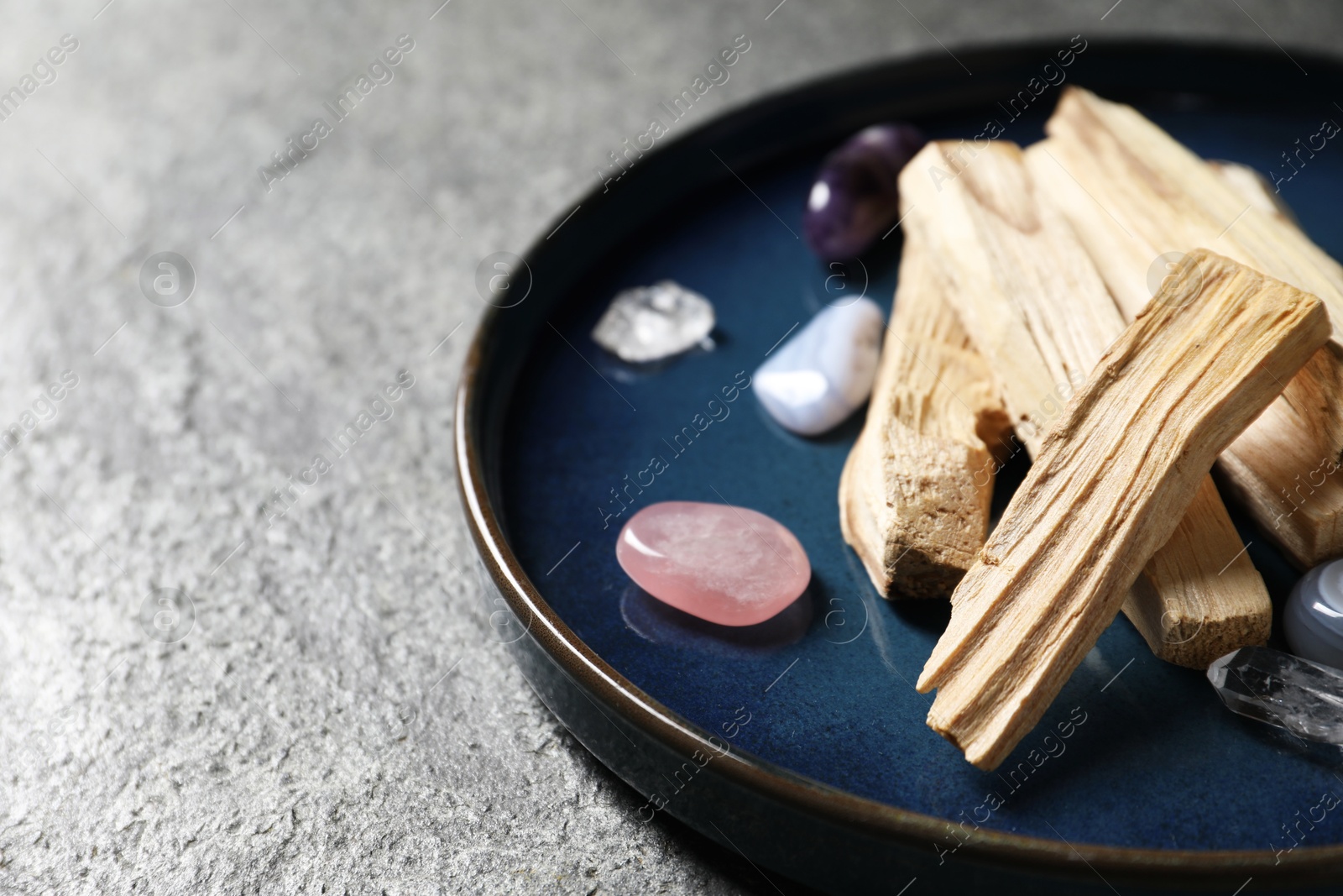 Photo of Palo santo sticks and gemstones on grey table, closeup