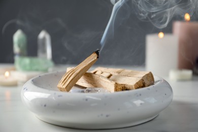 Photo of Smoldering palo santo stick, gemstones and burning candles on white table, closeup