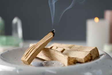 Photo of Smoldering palo santo stick and gemstones on table, closeup