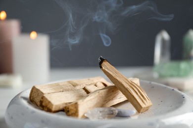 Photo of Smoldering palo santo stick and gemstones on table, closeup