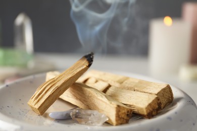 Photo of Smoldering palo santo stick and gemstones on table, closeup