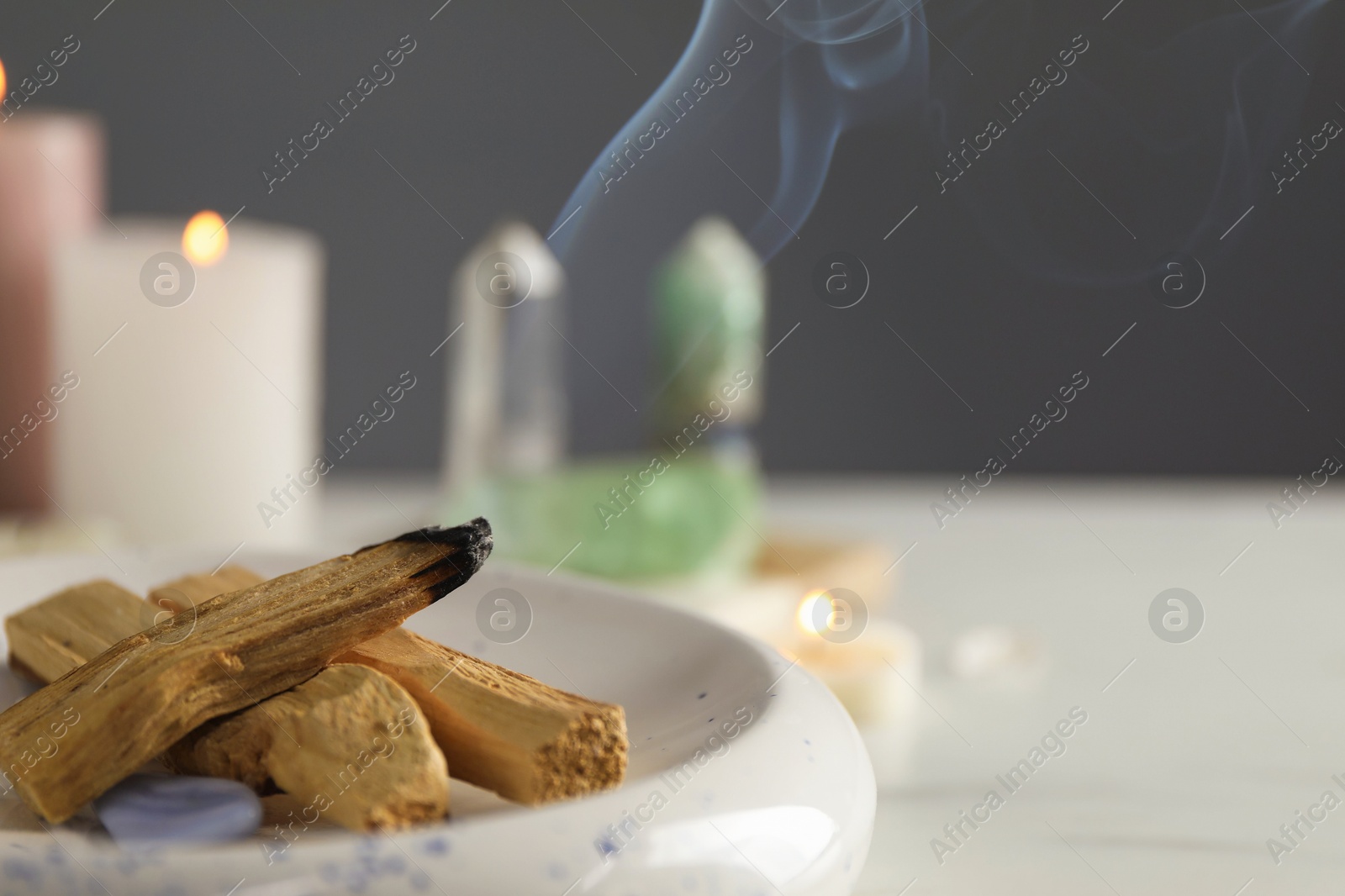 Photo of Smoldering palo santo stick and gemstone on table, closeup. Space for text