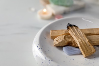 Photo of Smoldering palo santo stick and gemstone on table, closeup. Space for text