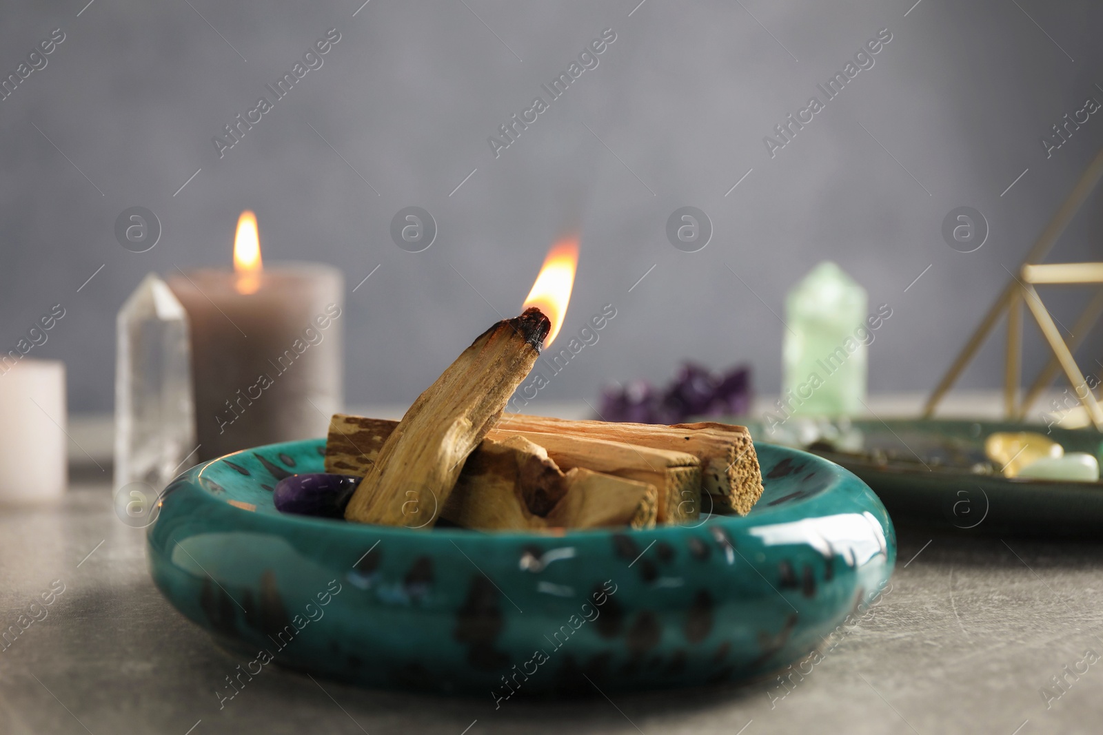 Photo of Burning palo santo stick and gemstone on grey table, closeup