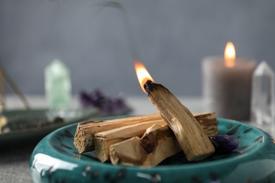 Photo of Smoldering palo santo stick and gemstone on table, closeup