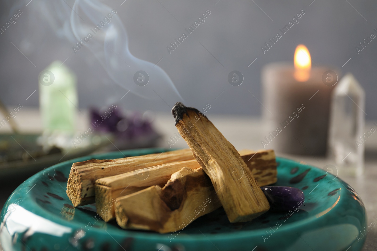 Photo of Smoldering palo santo stick and gemstone on table, closeup