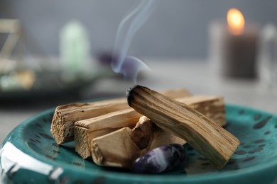 Photo of Smoldering palo santo stick and gemstone on table, closeup