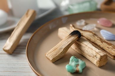 Photo of Burnt palo santo stick and gemstones on wooden table, closeup