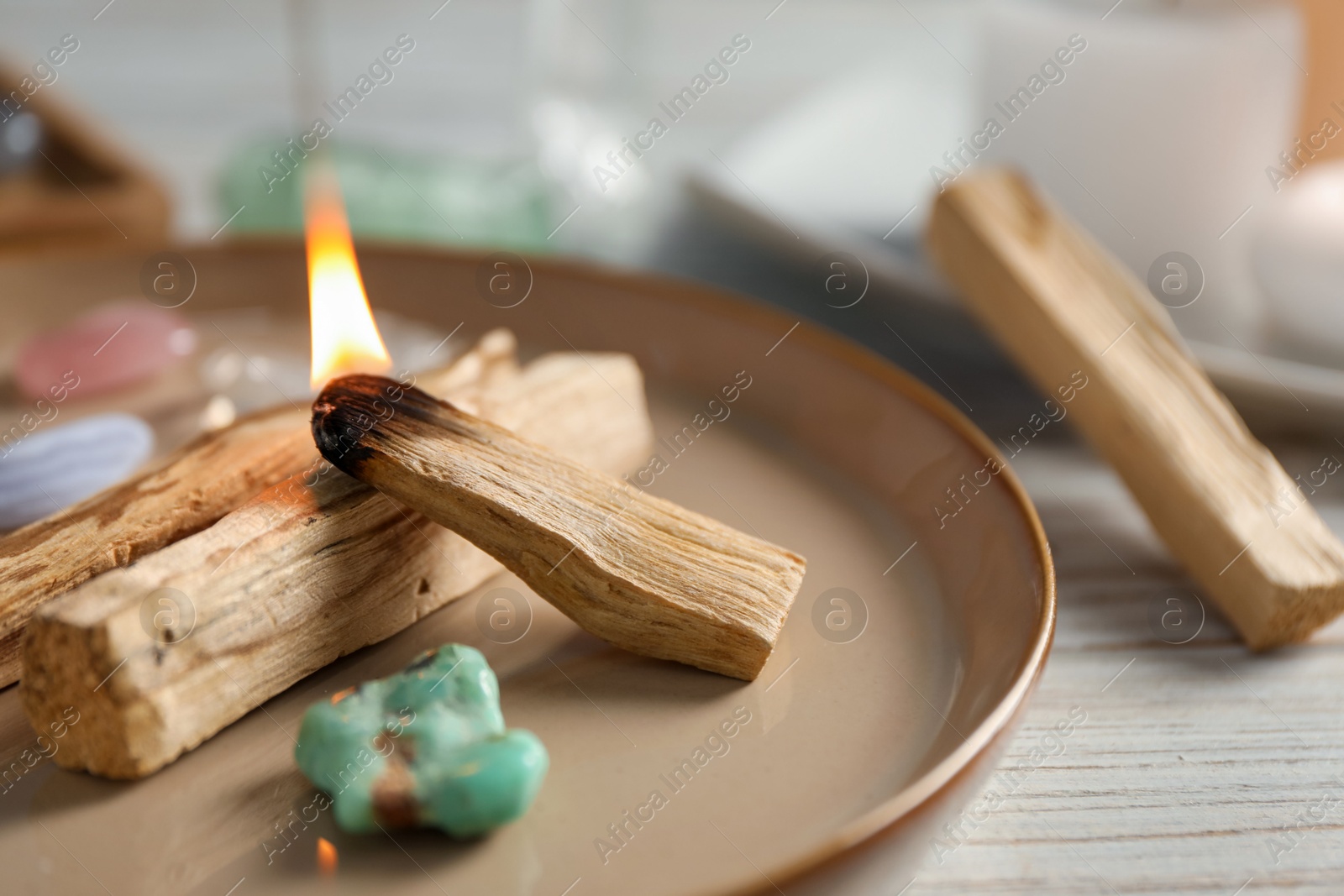 Photo of Burning palo santo stick and gemstones on wooden table, closeup