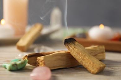 Photo of Smoldering palo santo stick and gemstones on wooden table, closeup