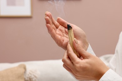 Photo of Woman with smoldering palo santo stick at home, closeup