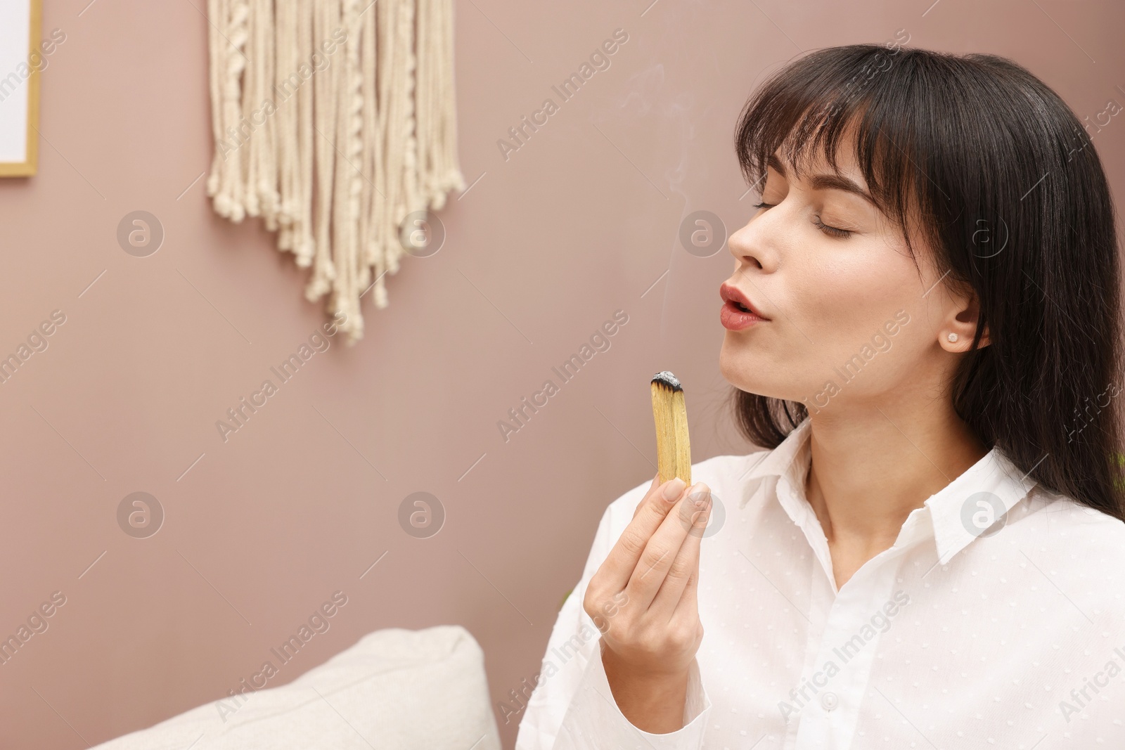 Photo of Woman with smoldering palo santo stick at home, space for text