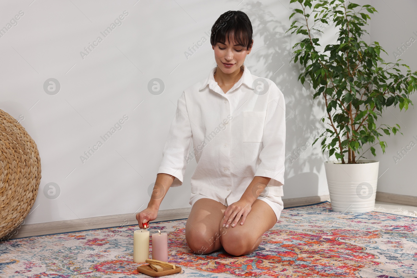 Photo of Woman lighting candle near palo santo sticks on floor at home, space for text