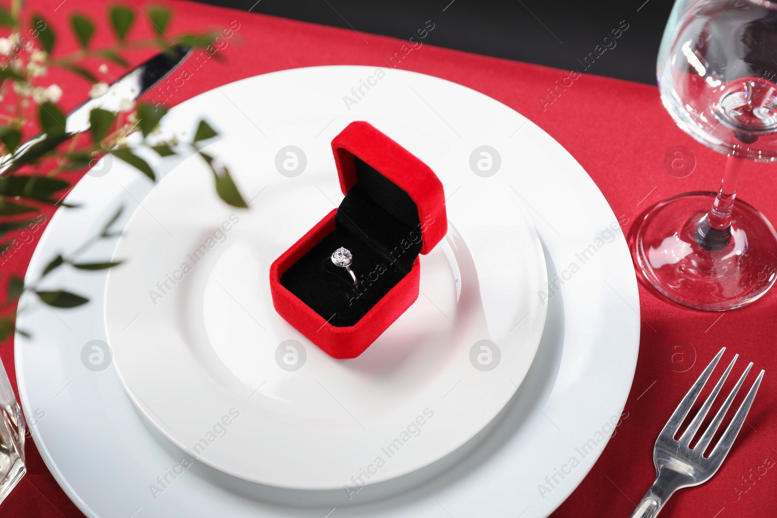 Photo of Beautiful engagement ring and setting for romantic dinner on red table, closeup