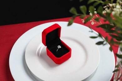 Photo of Beautiful engagement ring and setting for romantic dinner on red table, closeup