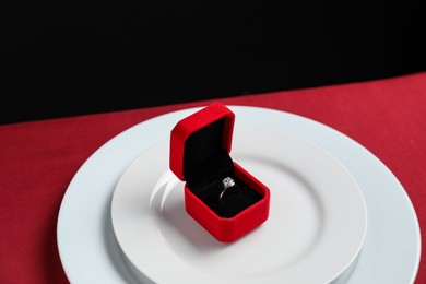 Photo of Beautiful engagement ring and setting for romantic dinner on red table, closeup