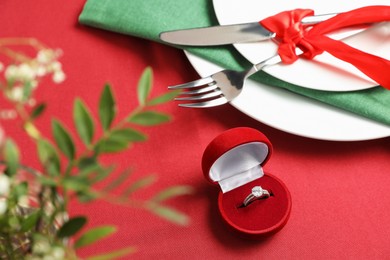 Photo of Beautiful engagement ring and setting for romantic dinner on red background, closeup