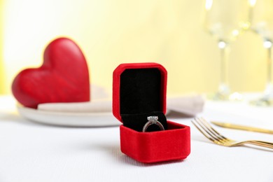 Photo of Beautiful engagement ring and setting for romantic dinner on white table, closeup