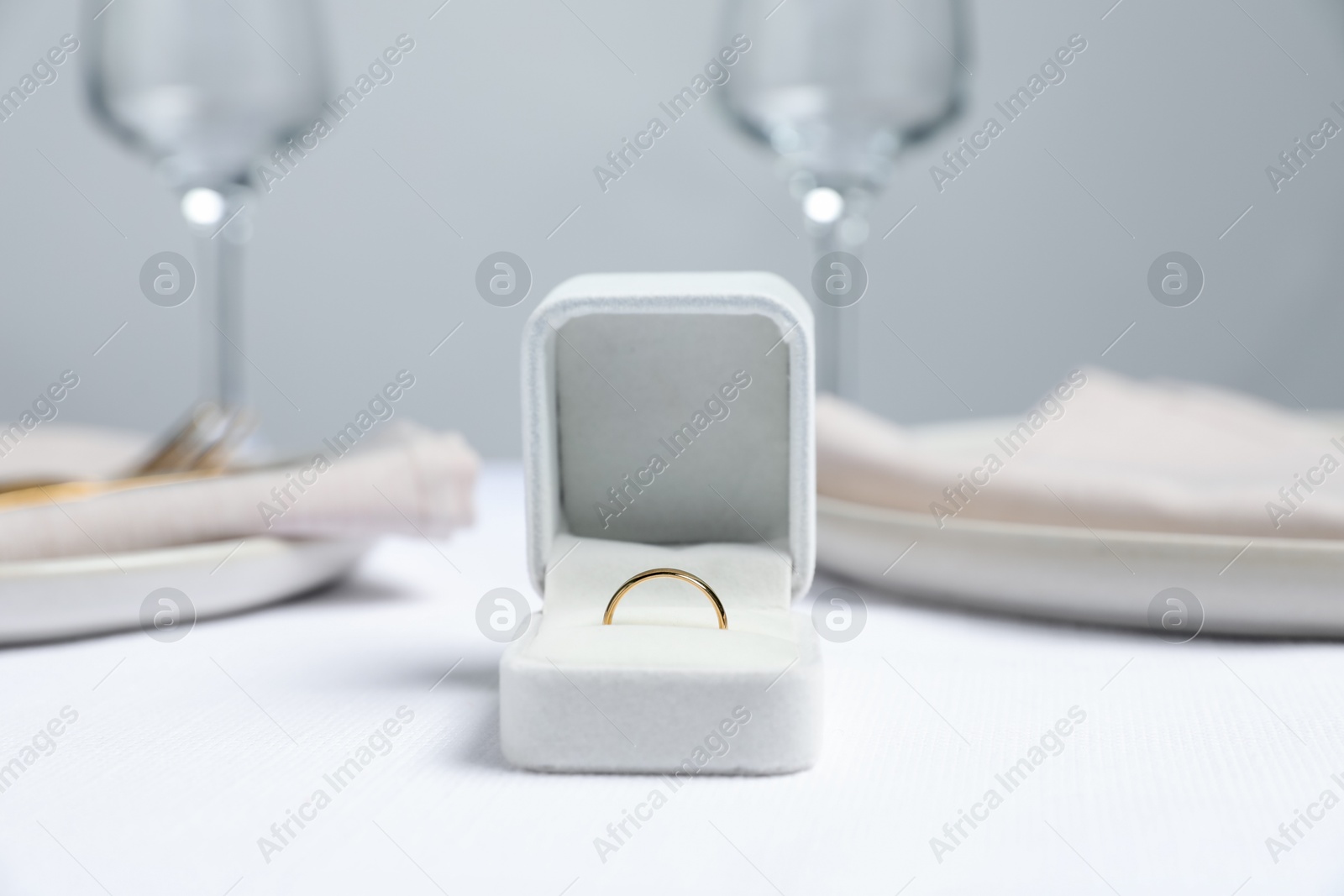 Photo of Beautiful engagement ring and setting for romantic dinner on white table, closeup