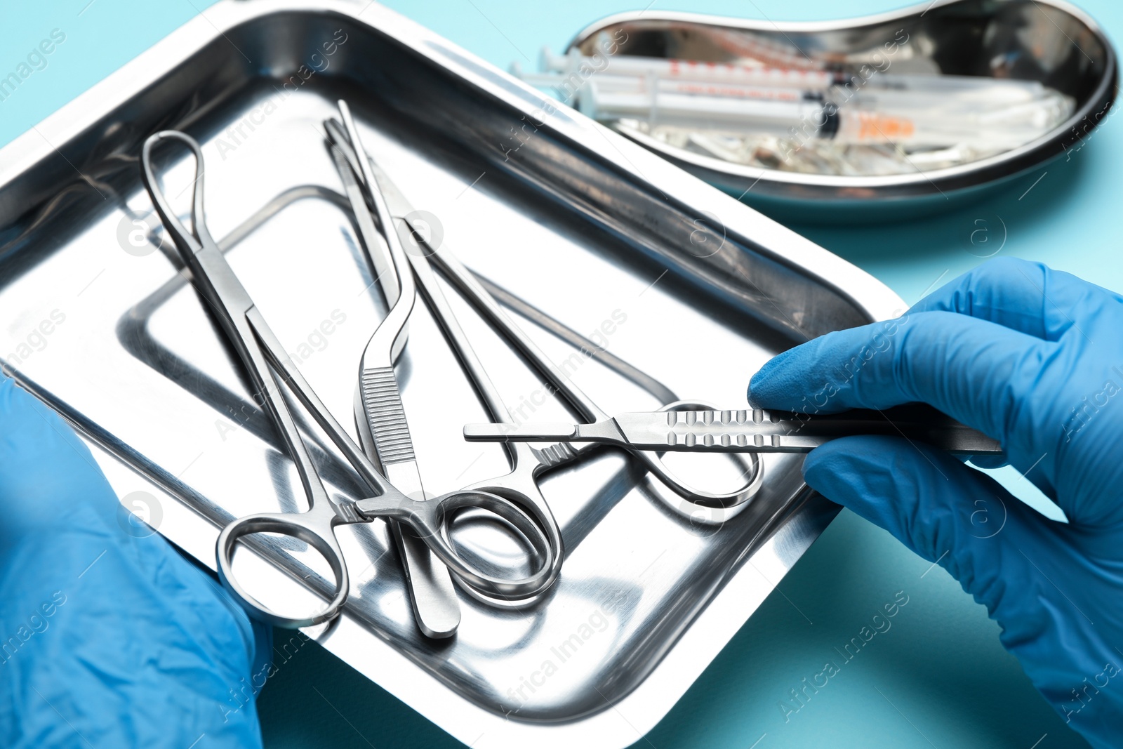 Photo of Doctor with different surgical tools on turquoise background, closeup