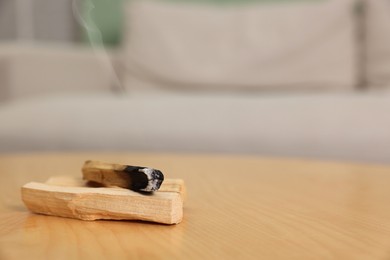 Photo of Burnt palo santo stick on wooden table indoors, space for text