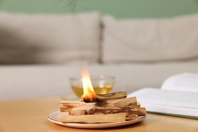 Photo of Palo santo sticks and burning one on wooden table indoors