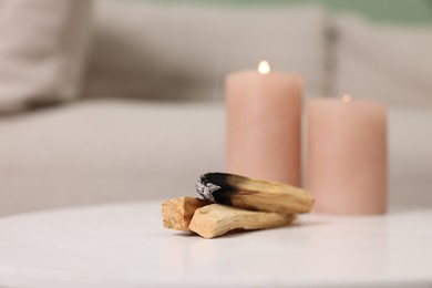 Photo of Palo santo sticks and burning candles on white table indoors, space for text