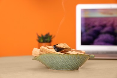 Photo of Palo santo sticks and smoldering one on wooden table against orange wall