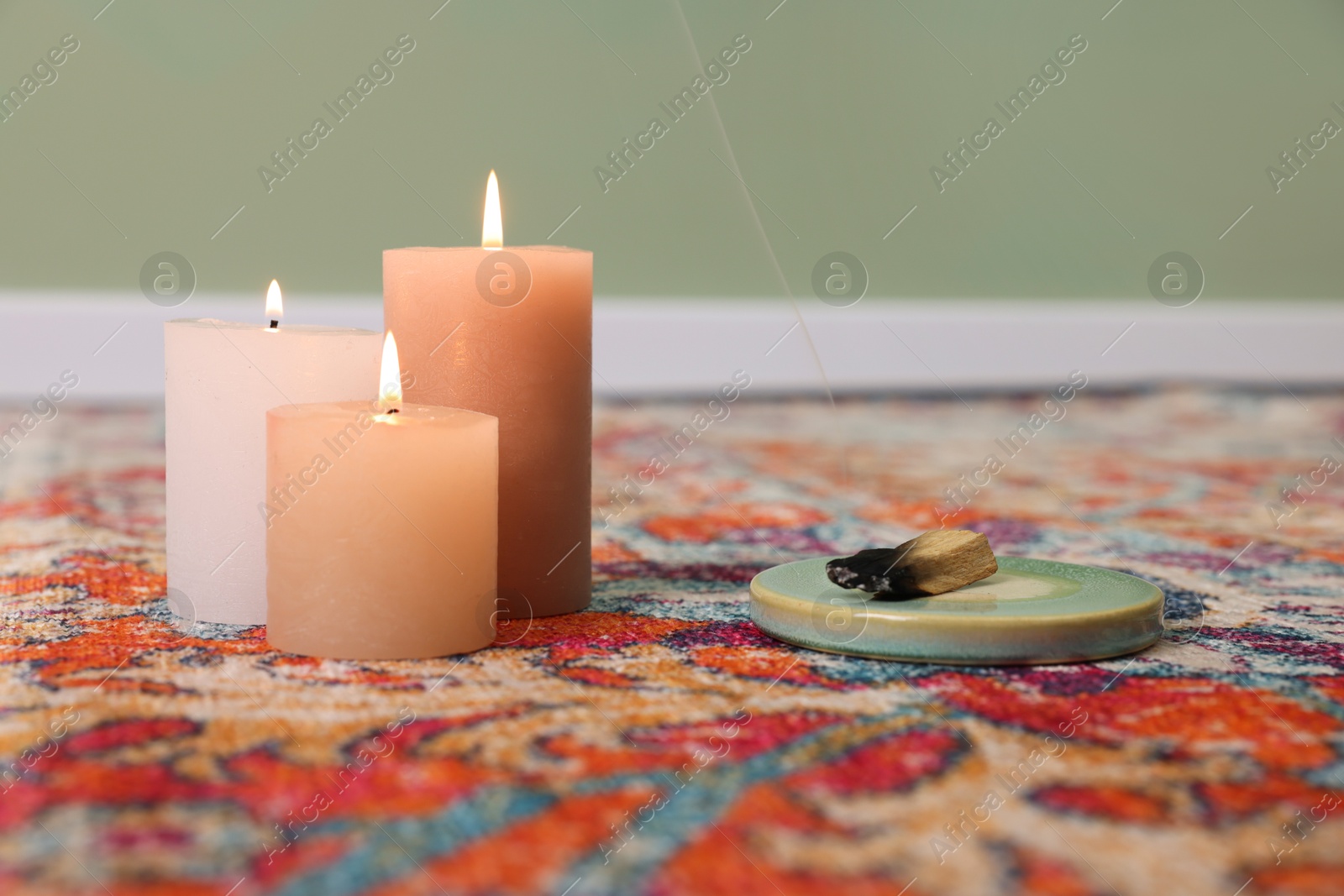 Photo of Palo santo sticks and burning candles on rug indoors, space for text