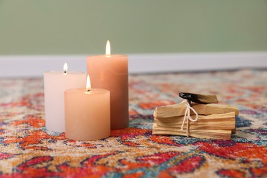 Photo of Palo santo sticks and burning candles on rug indoors, space for text