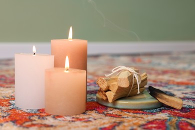 Photo of Palo santo sticks and burning candles on rug indoors, space for text