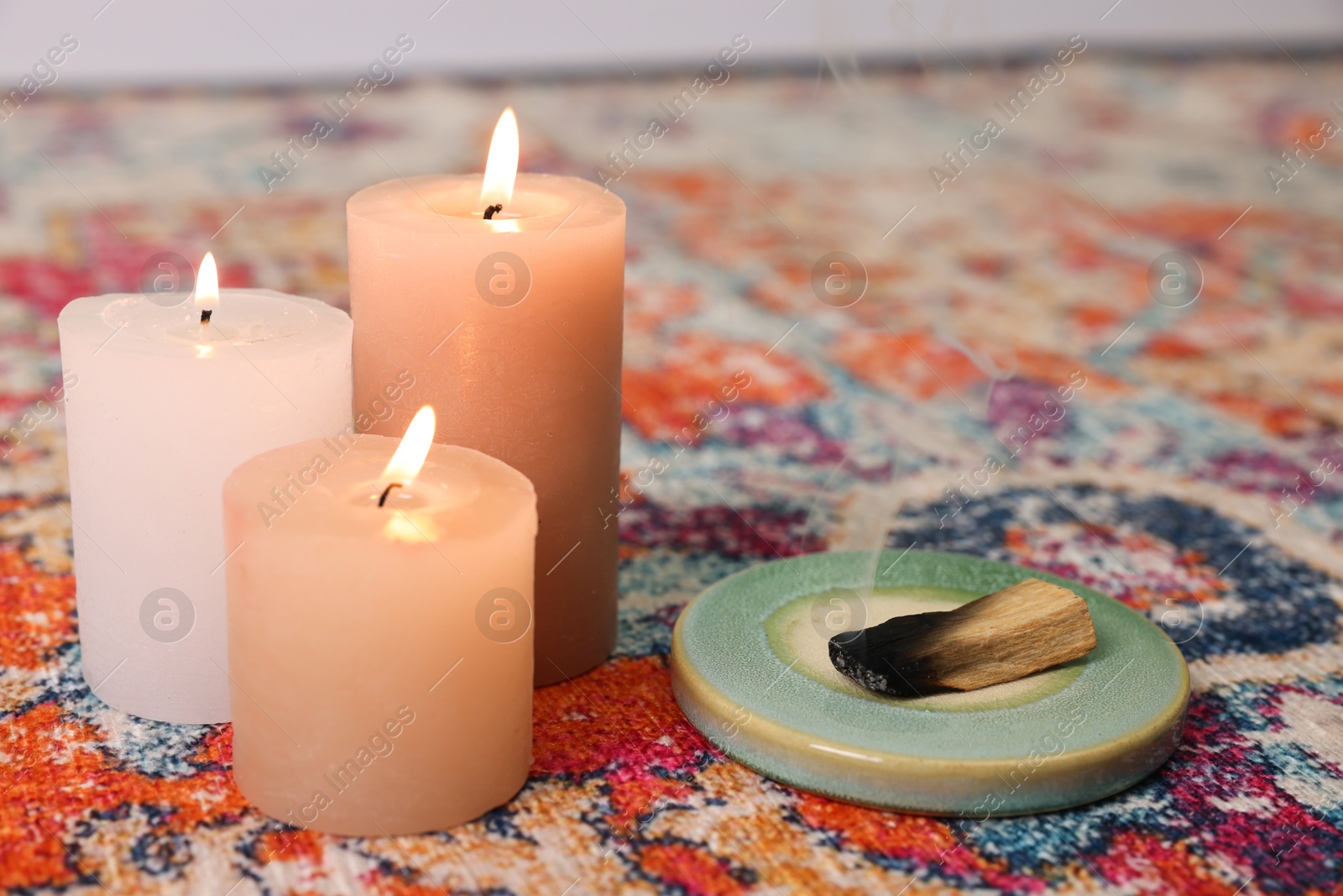 Photo of Palo santo sticks and burning candles on rug indoors, space for text