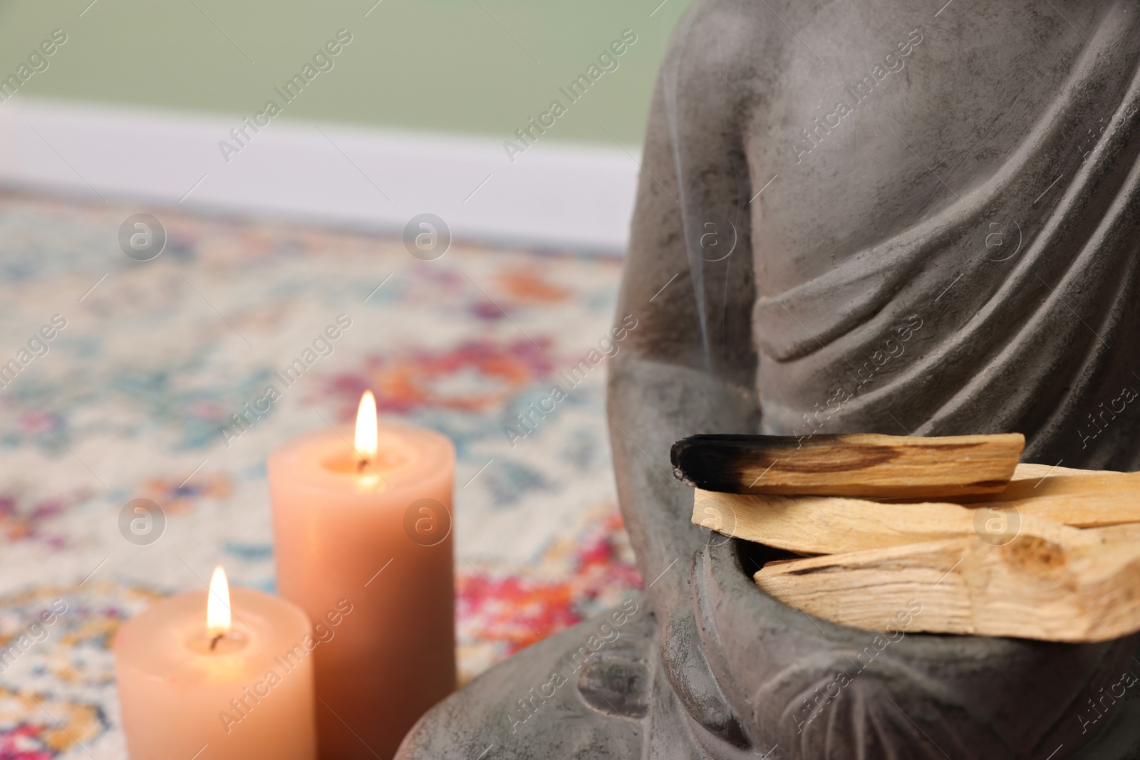 Photo of Buddha statue with palo santo sticks and burning candles indoors, closeup. Space for text