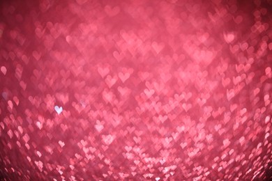 Photo of Romantic decor. Blurred view of heart shaped lights on pink background, bokeh effect