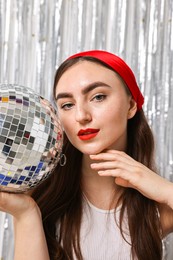 Photo of Portrait of beautiful young woman with disco ball against silver foil curtain