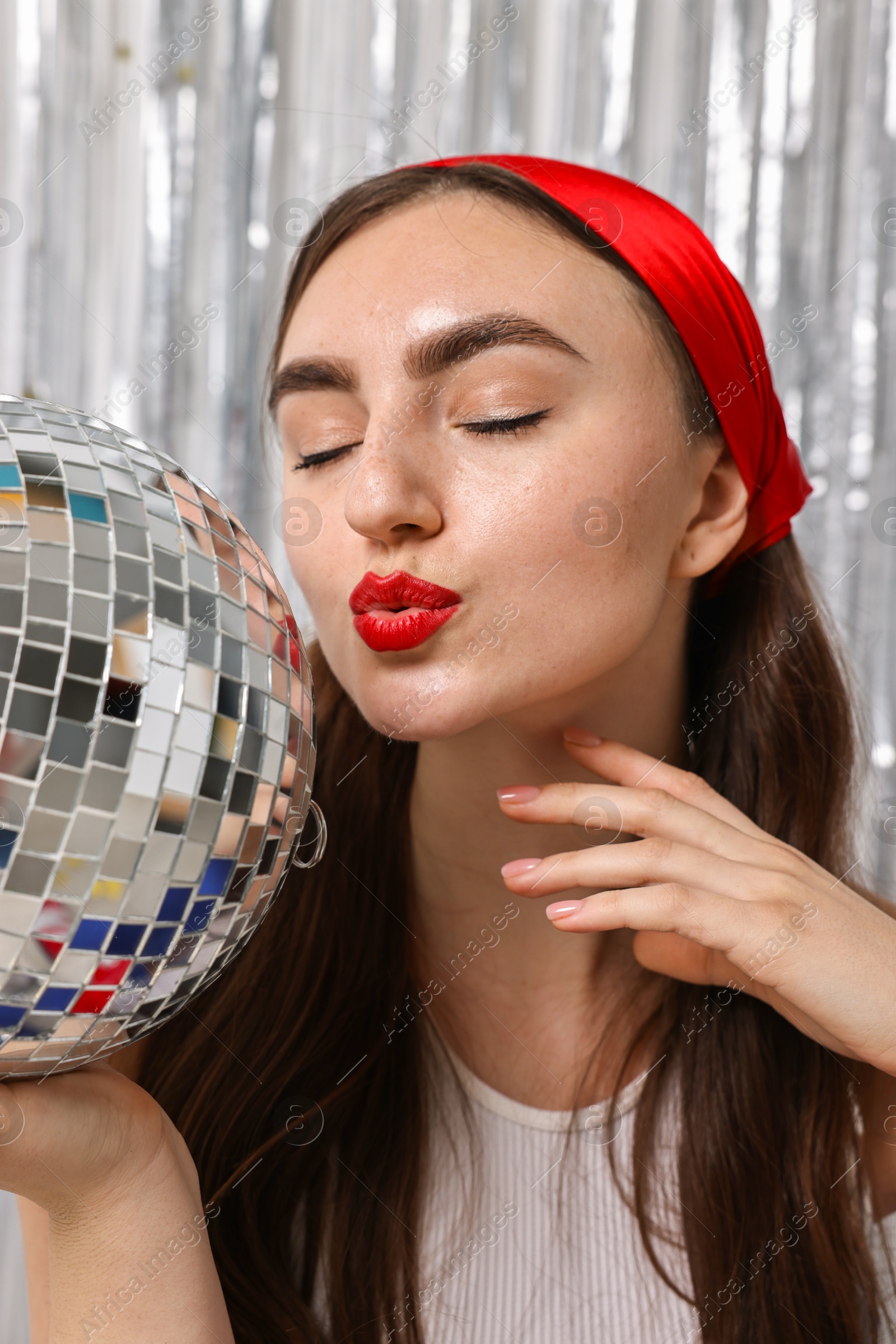 Photo of Portrait of beautiful young woman with disco ball against silver foil curtain