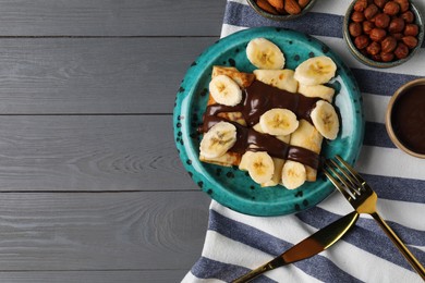 Photo of Delicious crepes with banana, nuts and chocolate sauce on grey wooden table, flat lay. Space for text